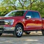 A new Ford truck for sale, a red 2021 Ford F-150, is parked in front of trees and a fence near Cincinnati, OH.