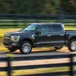 A black 2021 Ford F-150 Hybrid is driving past fenced in fields outside of Cincinnati, OH.