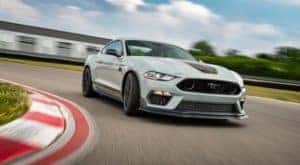 A white 2021 Ford Mustang Mach 1 is driving around a corner on a track near Cincinnati, OH.