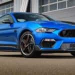 A blue 2021 Ford Mustang Mach 1 is parked in front of warehouse garage doors after leaving a Cincinnati car dealer.