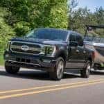 A black 2021 Ford F-150 from a local Ford dealership is towing a boat on a highway near Cincinnati.