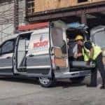 A white 2020 Ford Transit Connect Cargo is parked with an HVAC worker taking ducting out of the rear, after leaving the Ford commercial vehicle dealer.