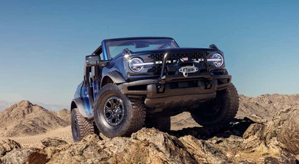 A blue 2021 Ford Bronco from a Cincinnati Ford Bronco dealer is shown from a low angle while parked off-road on rocks.