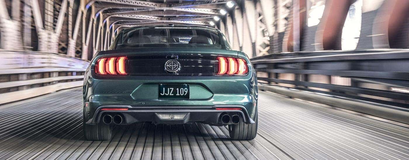 Rear view of a green 2019 Ford Mustang Bullitt driving on a metal bridge.