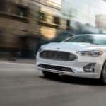 A white 2020 Ford Fusion is driving on a city street after leaving a Ford dealer in Cincinnati.