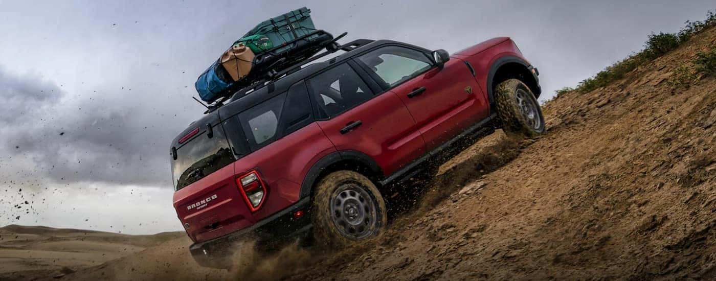 A red 2021 Ford Bronco Sport off-roading up a steep dirt hill with luggage on the roof rack