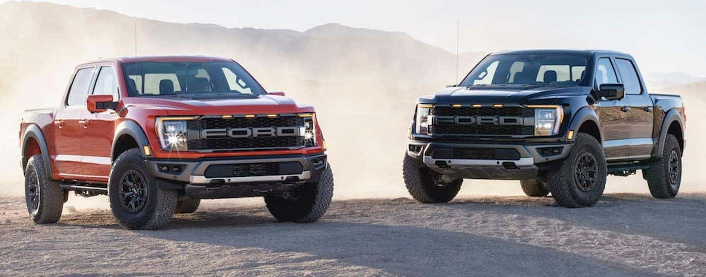Two 2021 Ford F-150 Raptors, one red and one black, parked in the desert.