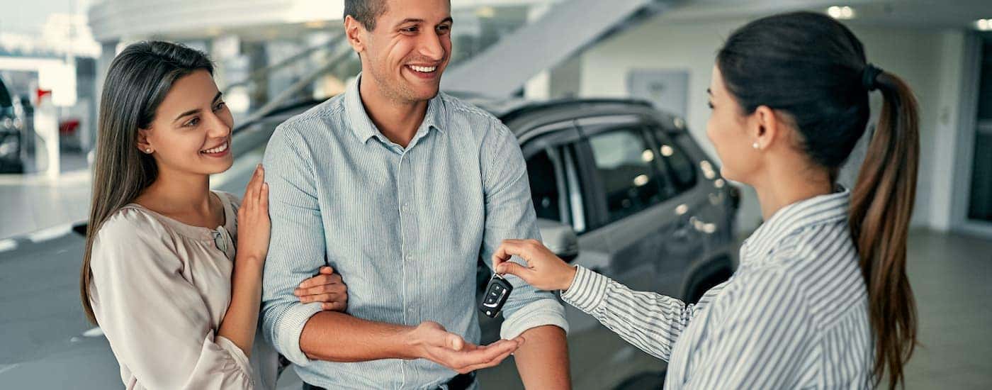 A saleswoman hands car keys to a smiling couple in the dealership showroom