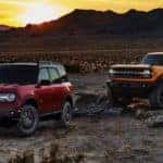 A red 2021 Ford Bronco Sport and a yellow Bronco 2 Door are parked in a desert at sunset.