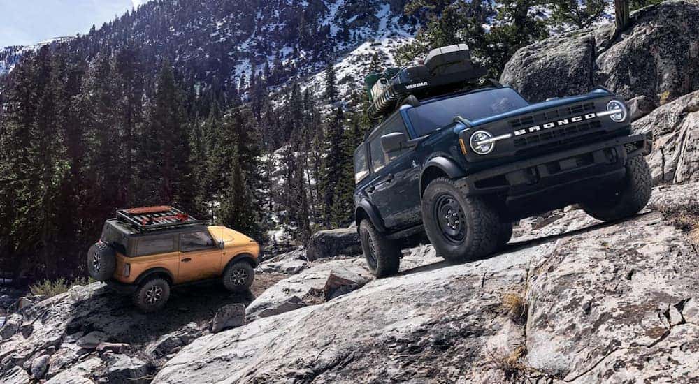 A yellow 2021 Ford Bronco 2-Door is following a black 4-Door on a rocky mountain trail.