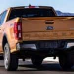 An orange 2019 Ford Ranger is shown from the rear driving on a road past snowy mountains.