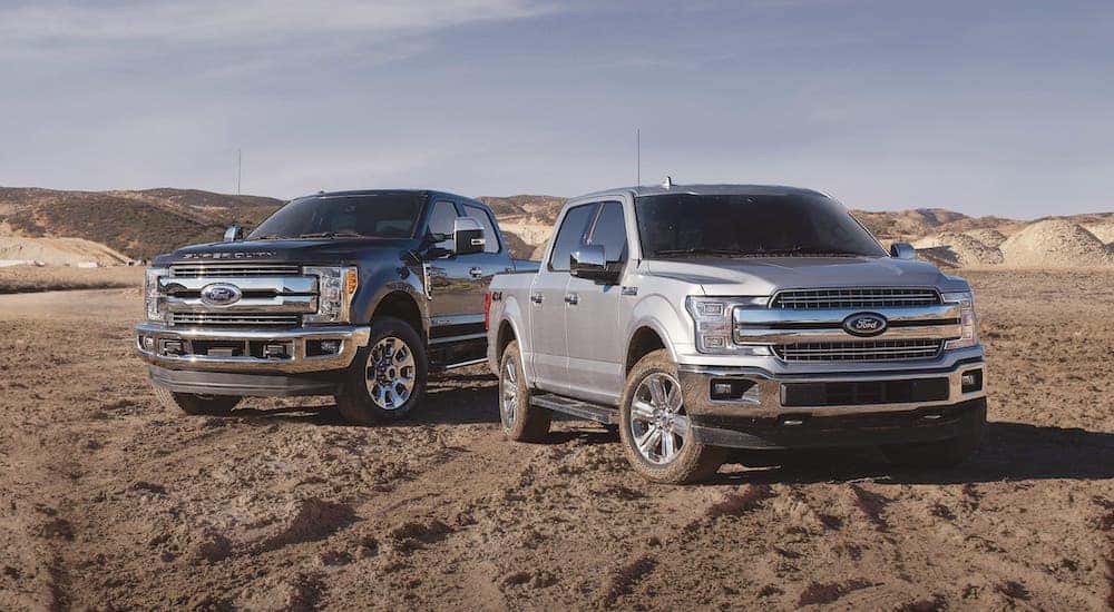 A black 2019 Ford F-250 Super Duty and a silver F-150 are parked in a dirt field.