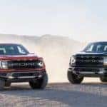 A red and a black 2021 Ford F-150 Raptor are parked on sand and will be coming to Cincinnati Ford F-150 dealers in the summer of 2021.
