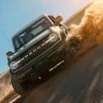 A gray 2021 Ford Bronco 4-door is shown at an angle driving on a sand dune.