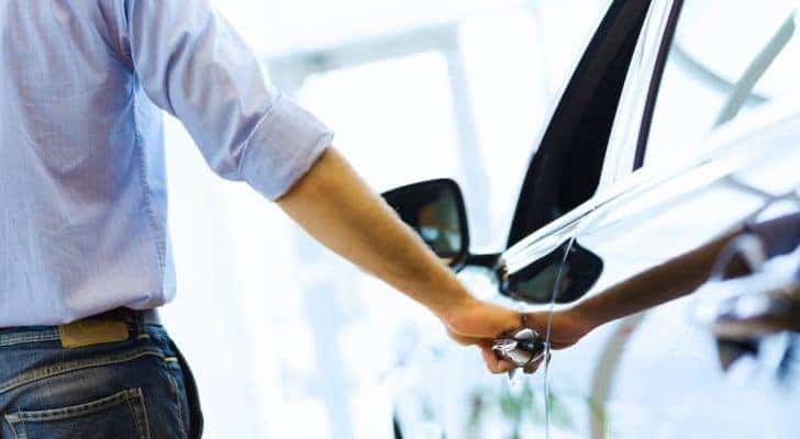 A close up shows a person holding a car door handle.