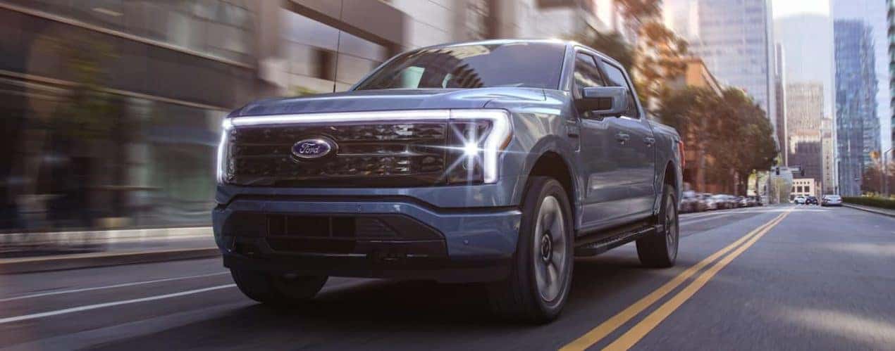 A blue 2022 Ford F-150 Lightning is shown driving through a city.