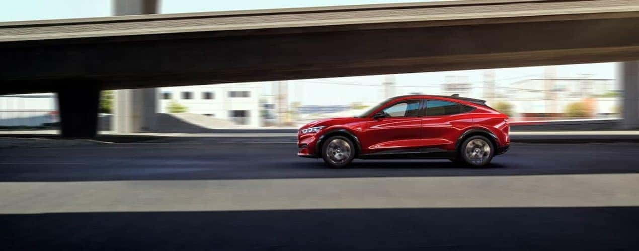 A red 2022 Ford Mustang Mach-E Premium is shown from the side driving in front of a bridge.