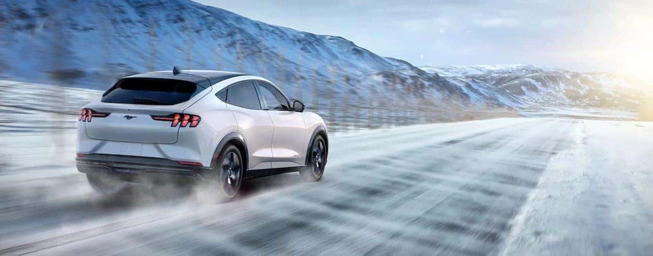 A white 2022 Ford Mustang Mach-E Premium is shown from the rear driving on a snowy road.