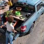 A woman is shown putting supplies into the bed of a blue 2022 Ford Maverick.