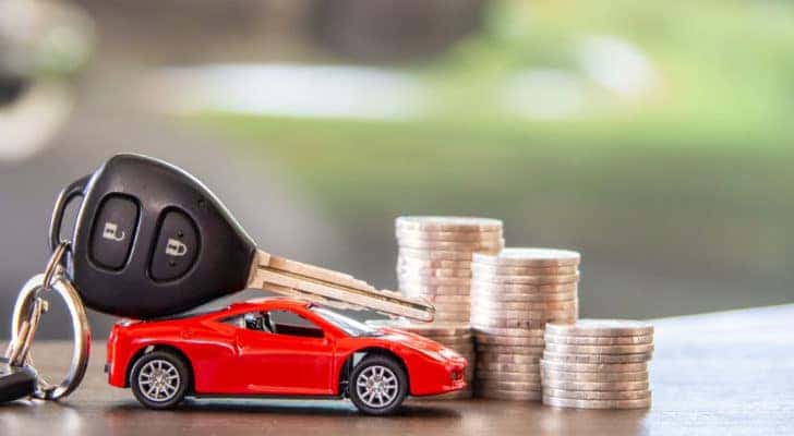 A toy car is shown next to a car key and stack of coins.