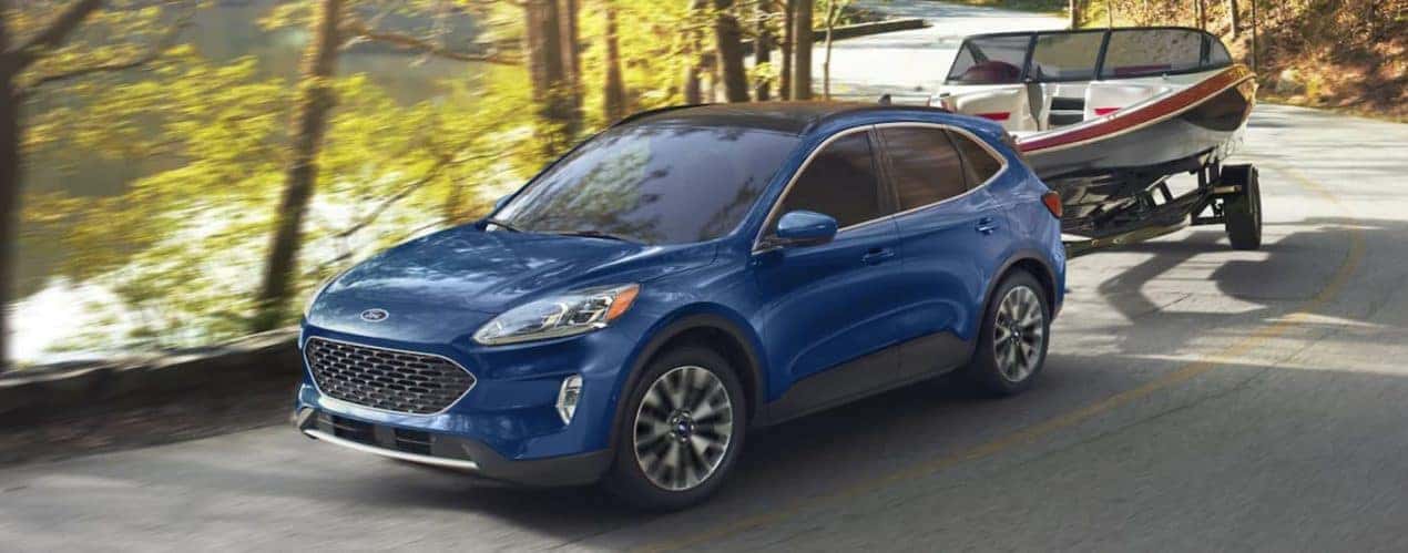 A blue 2022 Ford Escape is shown towing a boat along a tree lined road.