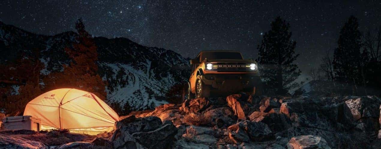 An orange 2022 Ford Bronco is shown parked in the mountains at night.