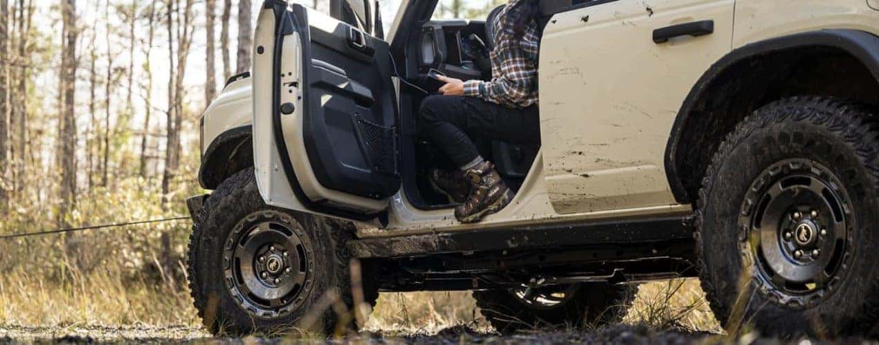 A tan 2022 Ford Bronco is shown from a low angle as a person gets out of the drivers side door.