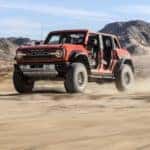An orange 2022 Ford Bronco Raptor is shown driving on dirt after visiting a Ford dealer in Cincinnati.
