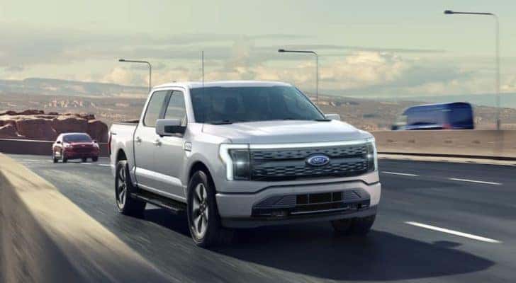 A grey 2022 Ford F-150 Lightning is shown from the front driving on an open road.