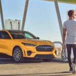 A yellow 2022 Mustang Mach-E is shown from the front at an angle with the driver approaching after leaving a Mason Ford dealer.