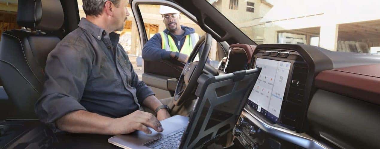 A man is shown speaking to a construction worker while sitting in a 2022 Ford F-150.