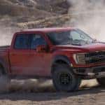 A red 2022 Ford F-150 Raptor kicks up dust while off-roading in the desert
