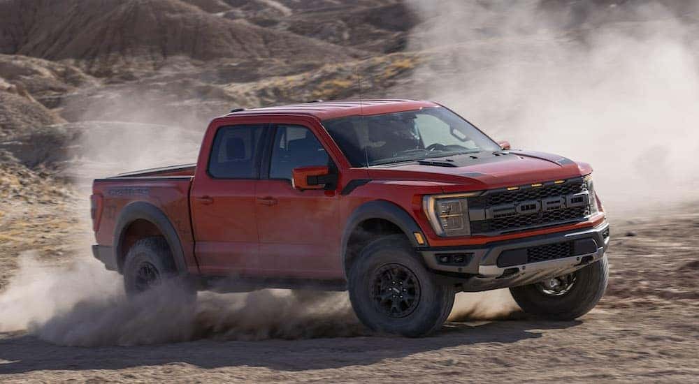 A red 2022 Ford F-150 Raptor kicks up dust while off-roading in the desert