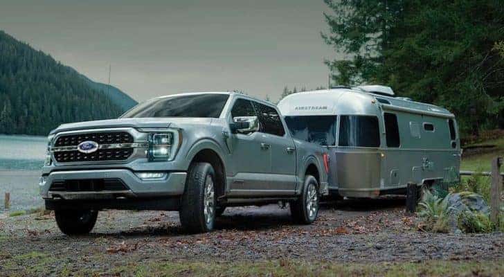 A silver 2022 Ford F-150 is shown towing an Airstream trailer near a lake.
