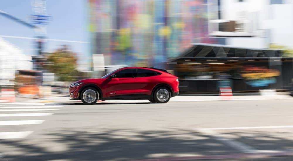 A red 2021 Ford Mustang Mach-E speeding down a colorful city street