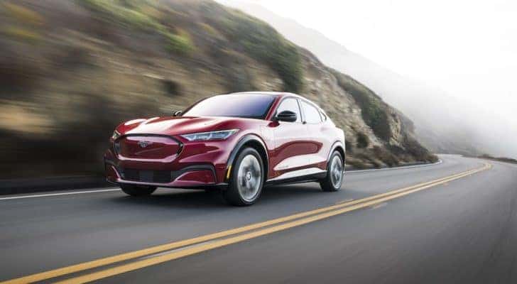 A red 2023 Ford Mustang Mach-E is shown driving past a rock face after leaving a Ford Mach-E dealer.