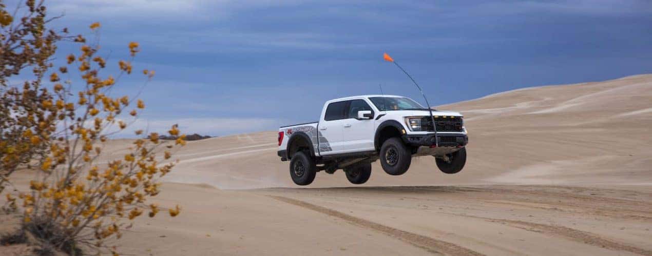 A white 2023 Ford F-150 Raptor R is shown from the side while jumping over a sand dune.