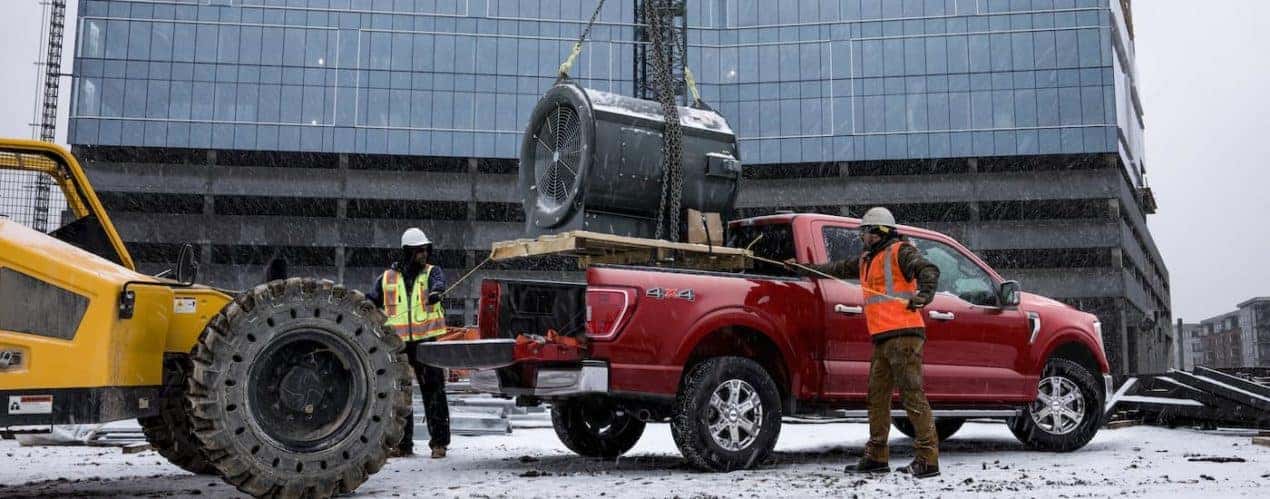 A large fan is shown being lowered into the bed of a red 2023 Ford F-150.