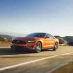 An orange 2018 Ford Mustang driving down an open desert road
