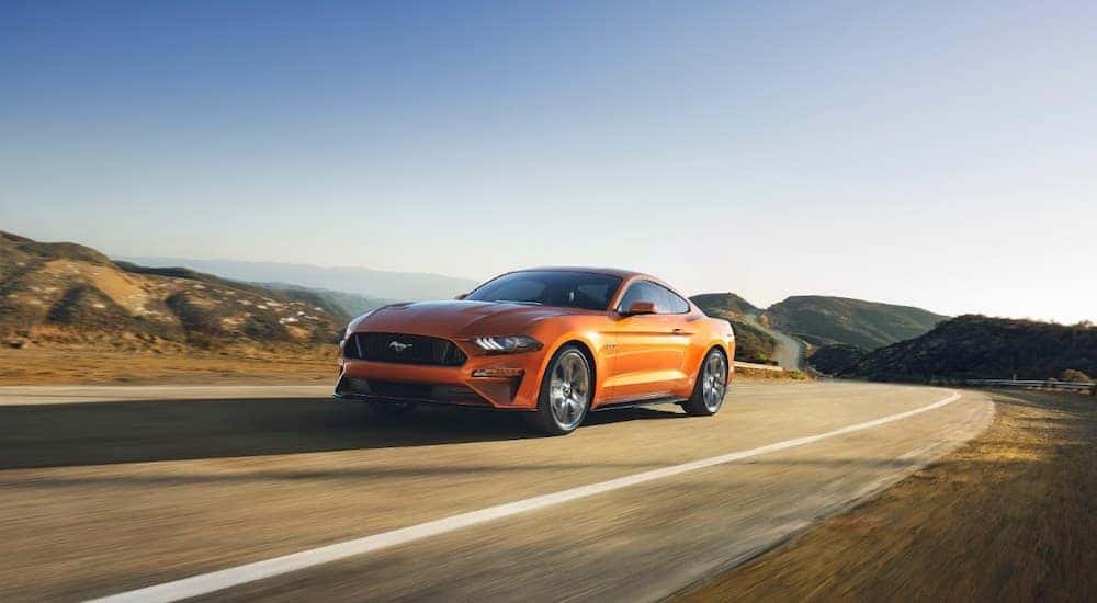 An orange 2018 Ford Mustang driving down an open desert road