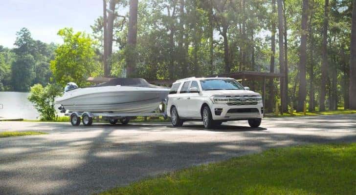 A white 2023 Ford Expedition towing a boat near a lake after leaving a Ford SUV dealer.