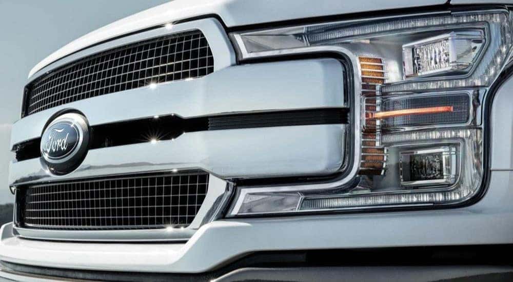 A close up of the grille and driver side headlight on a white 2020 Ford F-150.