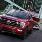 A red 2021 Ford F-150 towing a boat over a bridge.
