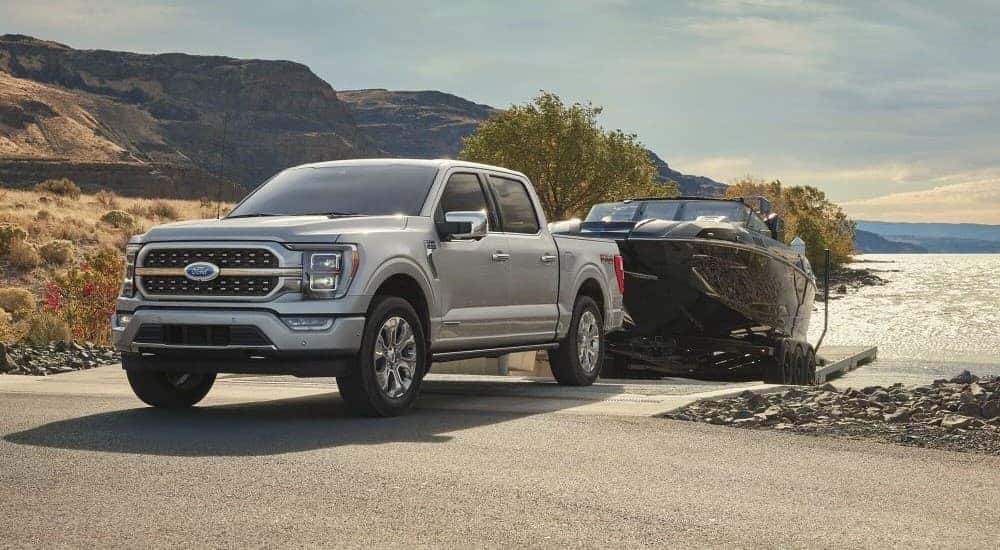 A silver 2023 Ford F-150 FX4 backing a boat into a lake in the mountains.