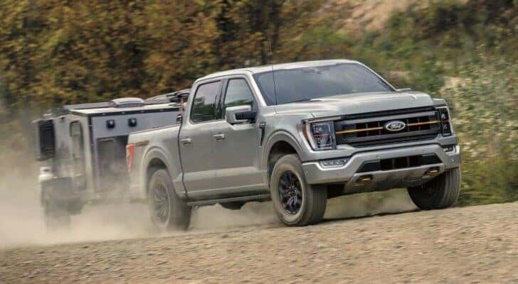 A grey 2023 Ford F-150 Tremor is shown towing a camper.
