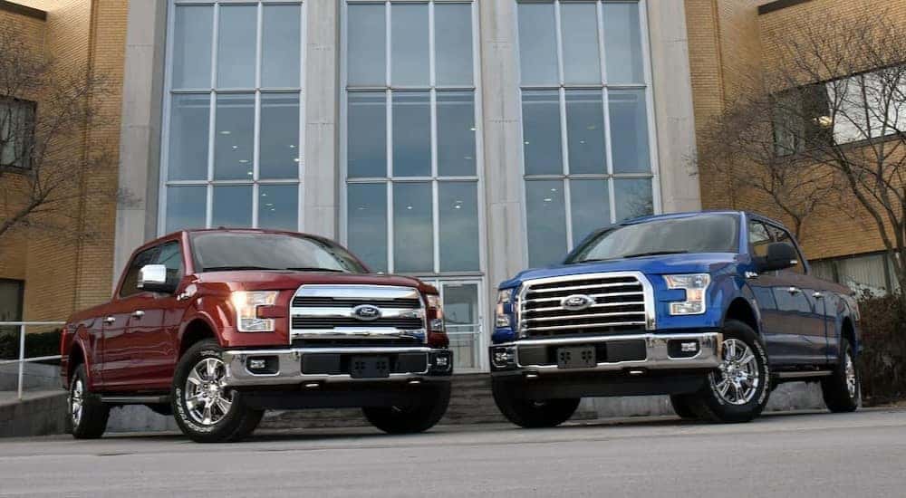 A red and a blue 2015 Ford F-150 parked in front of a building with large windows