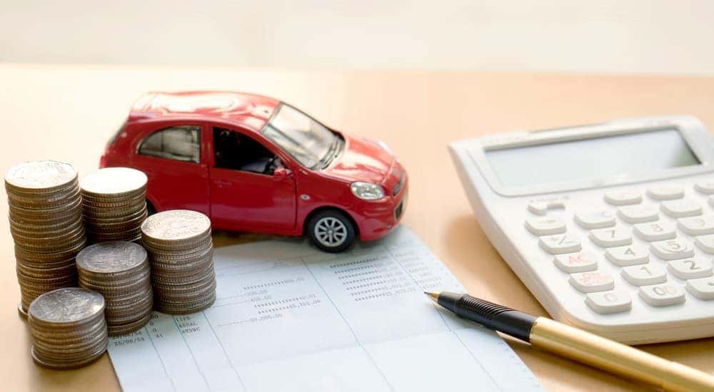 A toy red car is shown next to a set of coins and calculator.