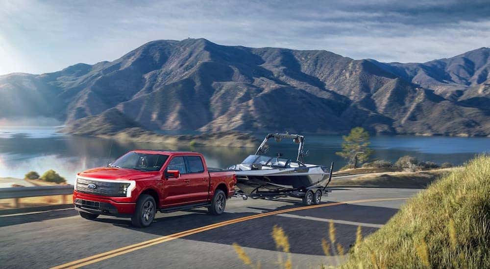 A red 2022 Ford F-150 Lightning is shown towing a boat after looking at a Ford Lightning for sale.