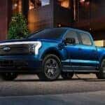 A blue 2022 Ford F-150 Lightning is shown charging on a driveway.
