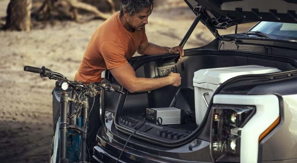 A person is shown using the outlet in the frunk of a 2023 Ford F-150 Lightning.